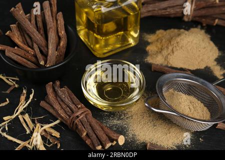 Dried sticks of licorice roots, powder and essential oil on black table Stock Photo
