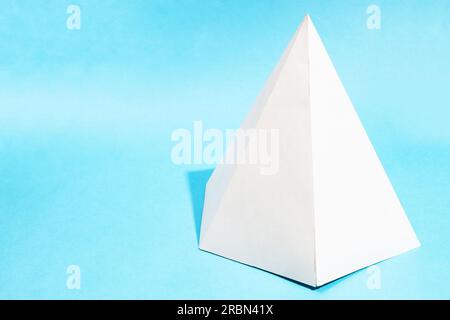 handcrafted paper hexagonal pyramid on turquoise blue background with copyspace Stock Photo