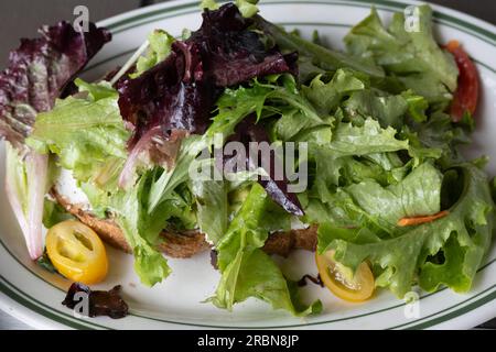 Raw lettuce and tomato salad over avocado toast, dinner angle view and close-up in a restaurant setting, healthy low-calorie meal Stock Photo