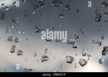 Rain drops on glass windscreen window close-up with cloudy blurred background. Moody rainy pattern Stock Photo