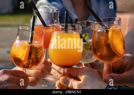 Close up of hands holding and toasting Aperol Spritz cocktail glasses at Stadtstrand bar, Wertheim, Spessart Mainland, Franconia, Baden-Wuerttemberg, Stock Photo