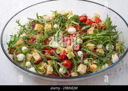 Baked cherry tomatoes, rucola, croutons, red onion, garlic, spices and cheese in a glass baking dish on a light gray background, top view. cooking Stock Photo