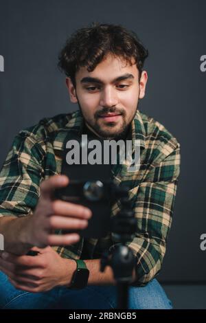 Bearded male photographer in checkered shirt and blue jeans looking at camera while taking photo on black background Stock Photo