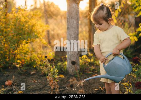 Little girl watering flowers in the garden against sunset light. Stock Photo