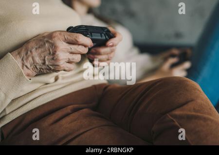 From above of crop anonymous caucasian woman sitting on sofa and playing video game with joystick Stock Photo