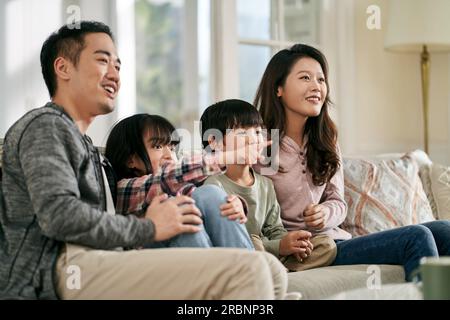 happy asian family with two children sitting on couch at home watching tv together Stock Photo