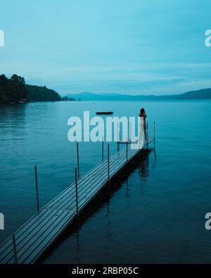 Person on a dock on a gloomy blue evening on Lake George in Silver Bay, New York Stock Photo