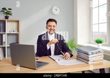 Young business man working at the desk on his workplace at office, looking at the camera smiling. Stock Photo