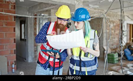 Man and woman builders using touchpad reading house project at construction site Stock Photo