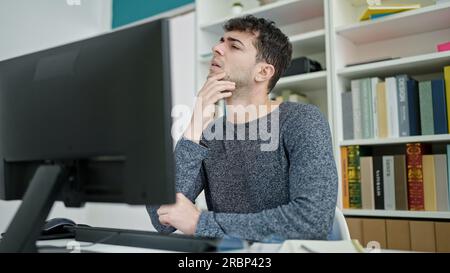 Young hispanic man using computer thinking at library university Stock Photo