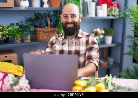 Young bald man florist smiling confident using laptop at flower shop Stock Photo