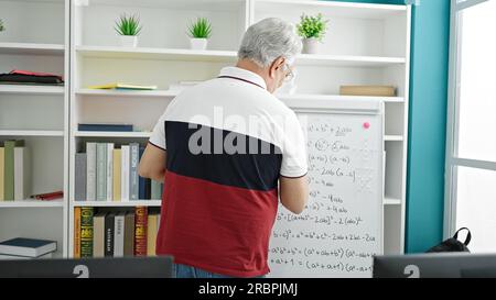 Middle age man with grey hair teaching maths on magnetic board at university classroom Stock Photo