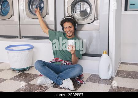 Guy Using Phone Listening Music While Doing Laundry At Laundromat Stock Photo