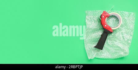 Packing tape dispenser and bubble wrap on green background with space for text Stock Photo