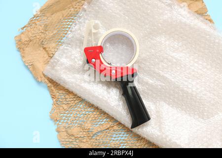 Packing tape dispenser, bubble wrap and paper on blue background Stock Photo