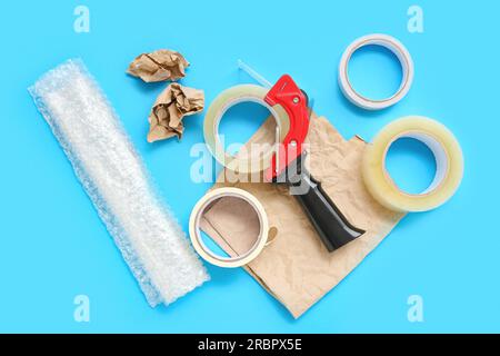 Adhesive tape rolls, dispenser, bubble wrap and paper on blue background Stock Photo