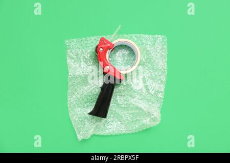 Packing tape dispenser and bubble wrap on green background Stock Photo