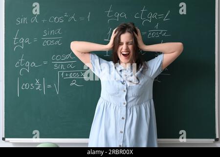 Stressed female Math teacher near chalkboard in classroom Stock Photo