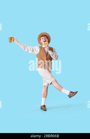 Young man in traditional German clothes with beer and pretzel dancing on blue background Stock Photo