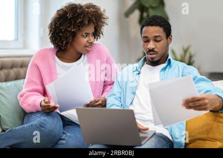 Confused young black husband and wife paying bills on Internet Stock Photo