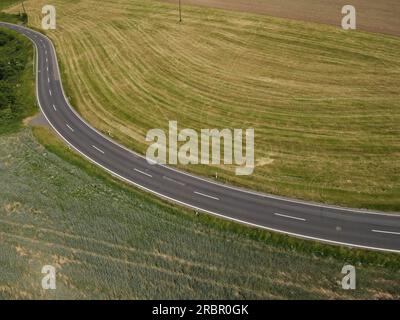 Rural curvy asphalt road in the landscape between grass fields in summer Stock Photo