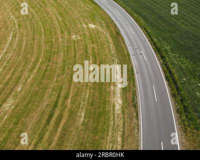 Drone view of a curved asphalt road with white stripes between grass fields in the landscape Stock Photo