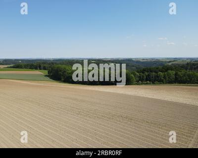 Drone view of brown plowed arable fields with dirt, trees and a blue sunny sky in summer Stock Photo