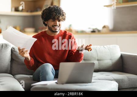 Stressed young indian freelancer guy working with papers and laptop at home Stock Photo