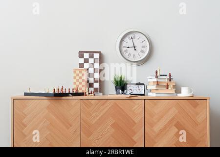 Chess boards with books and clock on chest of drawers in room Stock Photo