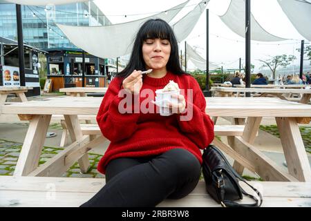 young latin woman of venezuelan ethnicity, sitting outdoors happy enjoying eating a vanilla and chocolate ice cream, food and drink concept. Stock Photo