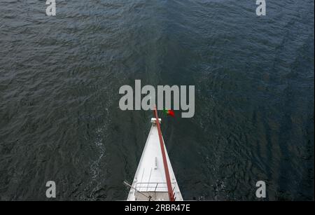 Aerial view from the stern of a tourist boat in the middle of the Douro river 'Rio Douro' with the Portuguese flag. City of Porto in Portugal. Stock Photo