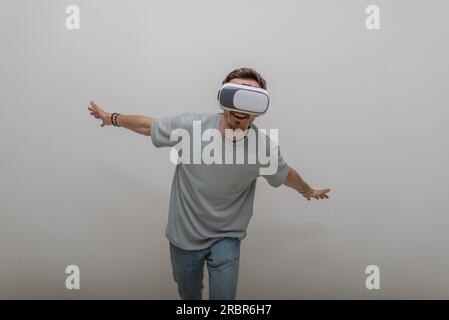 Futuristic man wearing virtual reality glasses interacts with the air in an isolated gray background. Stock Photo