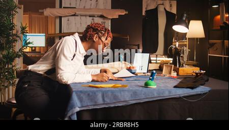 Seamstress using measuring tape in atelier, working with tailoring meter to measure fabric dimensions. Tailor preparing material to craft and design clothing items, textile industry. Stock Photo
