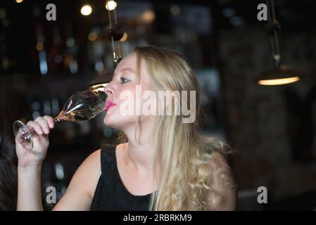 Beautiful blond woman enjoying a glass of champagne or prosecco in a nightclub or hotel on a night out celebrating a special occasion looking at the Stock Photo