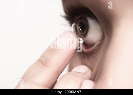 Woman about to place a disposable plastic contact lens in her eye to correct her vision has it balanced on the end of her finger in front of her eye Stock Photo