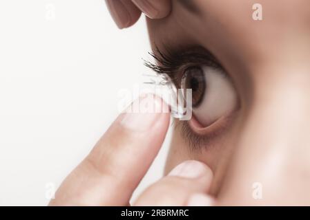 Woman about to place a disposable plastic contact lens in her eye to correct her vision has it balanced on the end of her finger in front of her eye Stock Photo