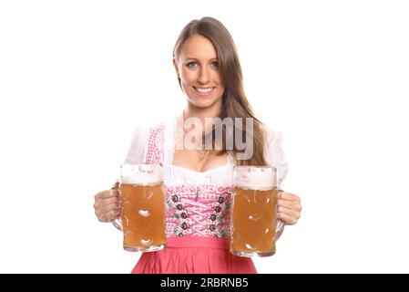 German or Bavarian waitress with her hair in pigtails wearing a traditional dirndl serving large glass tankards full of beer, Oktoberfest concept Stock Photo
