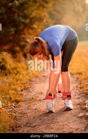 Pretty Smiling Young Woman adjusting her Ankle weigh cuffs, early warm summer morning outdoors Stock Photo