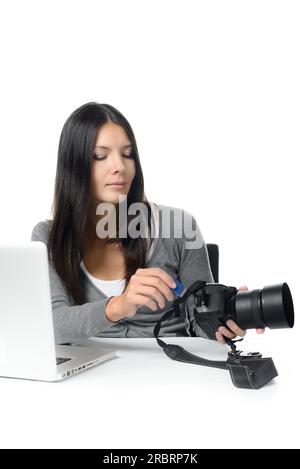 Female photographer inserting or removing a memory card in her professional dslr camera as she sits at a desk with her laptop ready to transfer Stock Photo