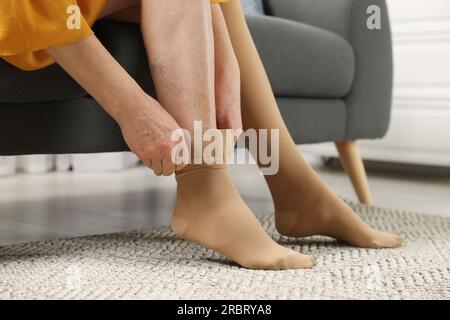 Woman putting on compression stocking in living room, closeup
