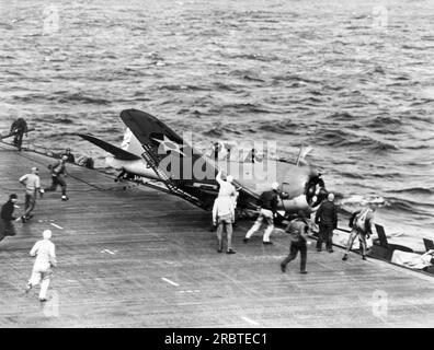 Pacific Ocean:  August, 1942 U.S. Navy scout bomber crashes while landing on the aircraft carrrier flight deck and ends up in the catwalk as ground crews rush to assist. Stock Photo