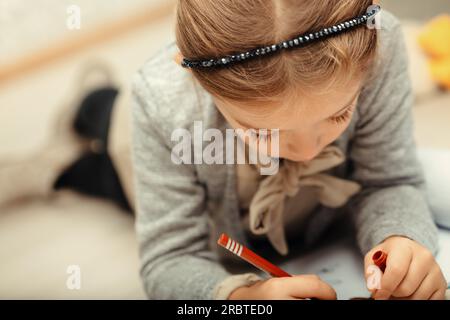 A small girl engrossed in coloring her sketchbooks. Imaginatively creating fantasy creatures and stories, or reinterpreting ones she's heard. Lying be Stock Photo