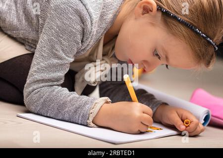 Little girl draws and colors, creating and reinterpreting stories. Engrossed in her play, lying on the floor, she's in a continuous process of growth. Stock Photo