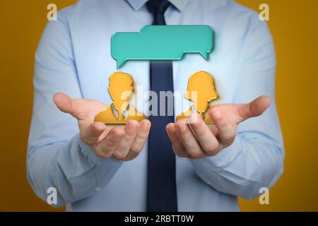 Productive dialogue, meaningful conversation. Businessman holding illustration of people with speech bubbles on dark gold background, closeup Stock Photo