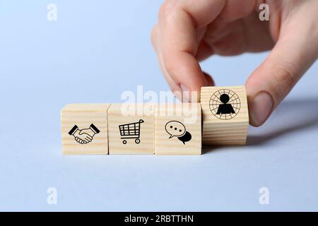 Professional buyer. Woman putting wooden cube with human icon on light background, closeup Stock Photo