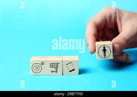 Professional buyer. Woman putting wooden cube with human icon on light blue background, closeup Stock Photo