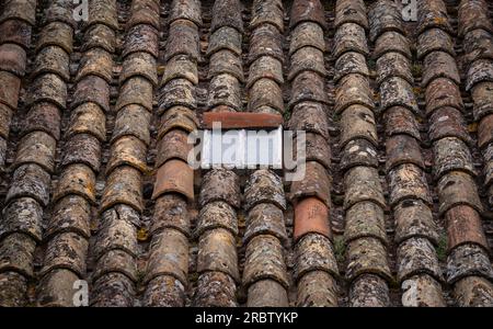 A rustic roof with old, discolored tiles, eroded by the rains and the passage of time on which lichens and mosses have grown. Stock Photo