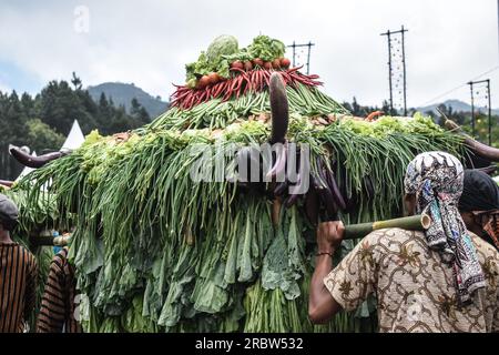 Men in traditional Javanese attire carry mountains of vegetables during the Mount Slamet festival Stock Photo