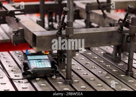 Workpieces and handheld CNC welding robot controller on welding table. Selective focus. Stock Photo