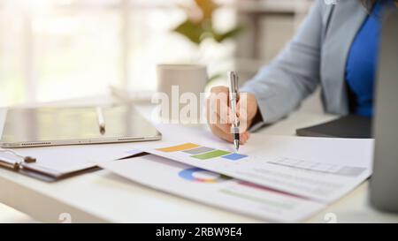 Close-up image of a professional businesswoman or female boss reviewing financial reports, pen pointing on a paper, working at her desk. Stock Photo